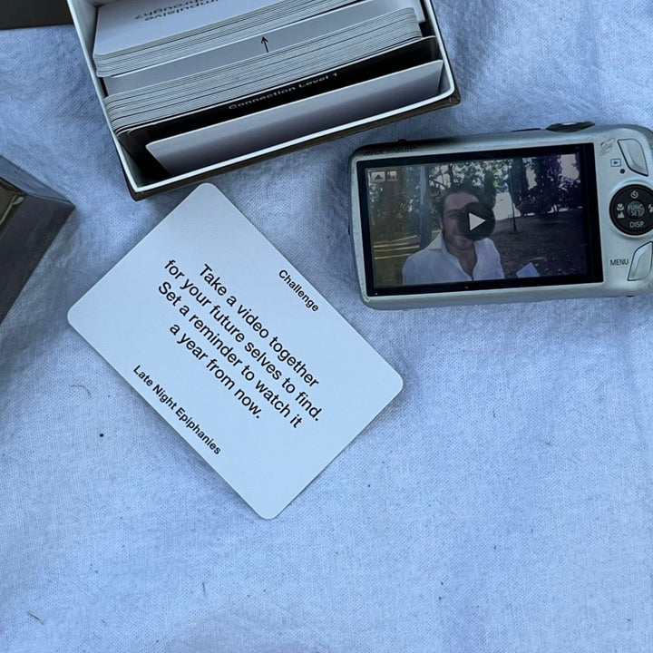 Challenge card from Level 3 of the Late Night Epiphanies card game next to a camera showing a video, encouraging players to create a memory for their future selves.