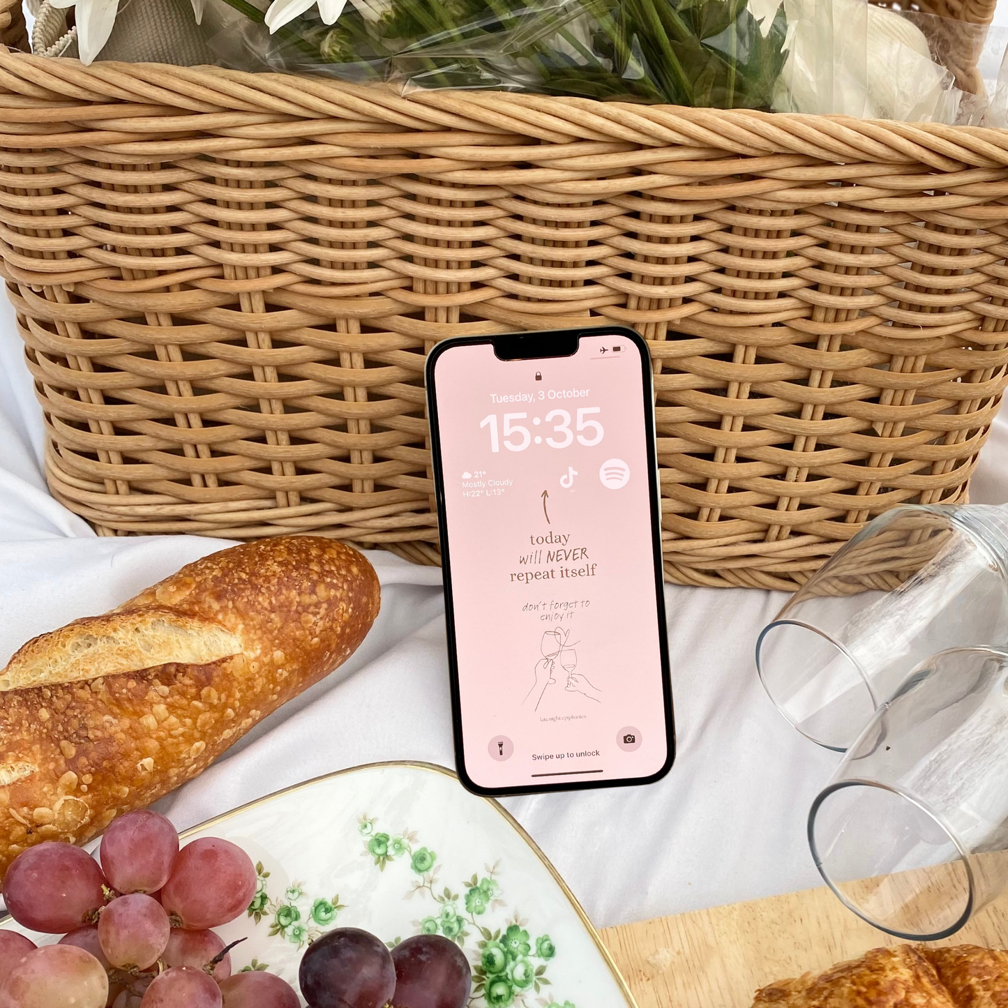 Image of an iPhone placed on a picnic with a Late Night Epiphanies wallpaper that says "today will never repeat itself, don't forget to enjoy it."